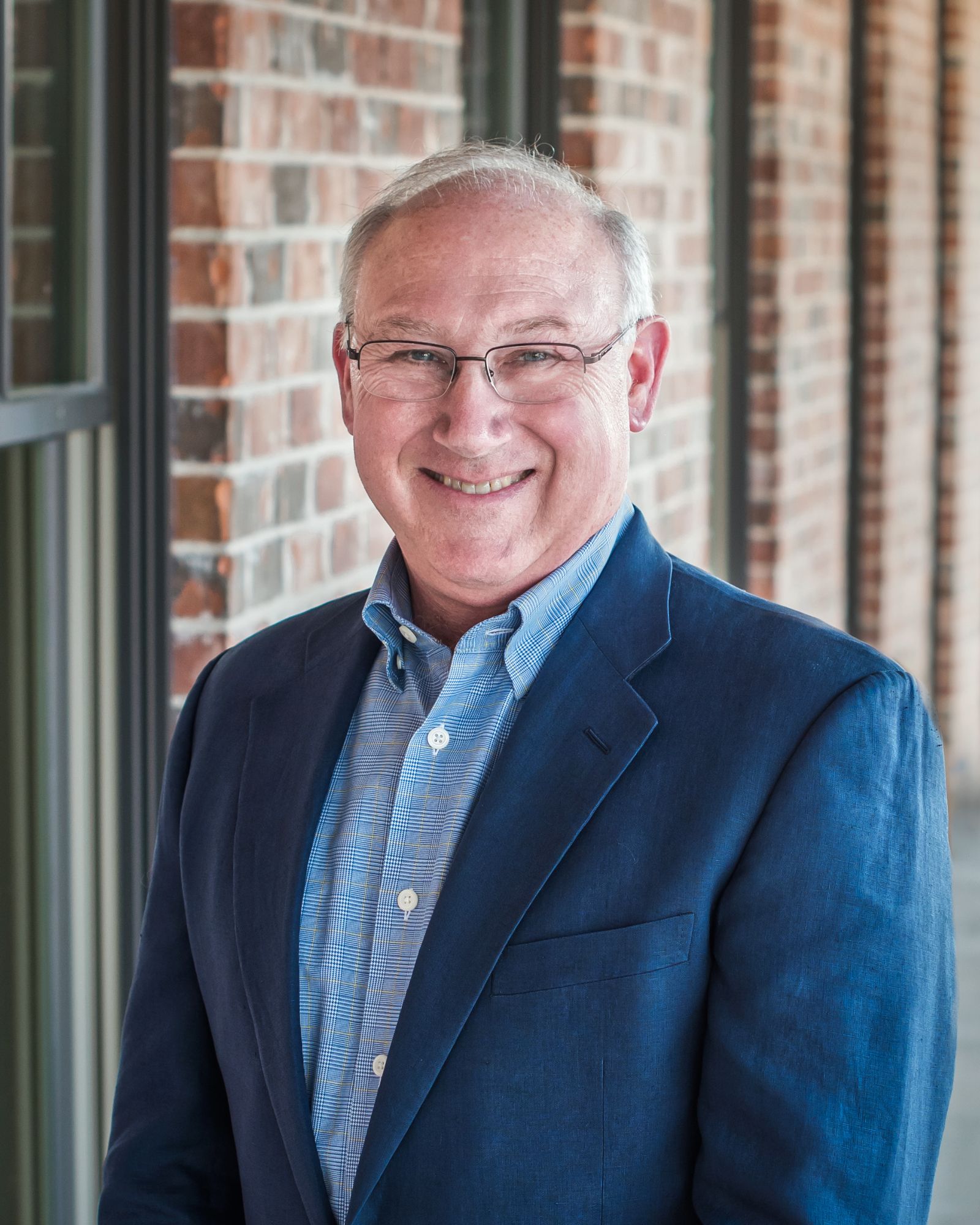 Dr. John Benton, board-certified orthodontist at Designer Smiles by Benton in Oxford, AL, wearing a blue blazer and standing in front of a brick wall